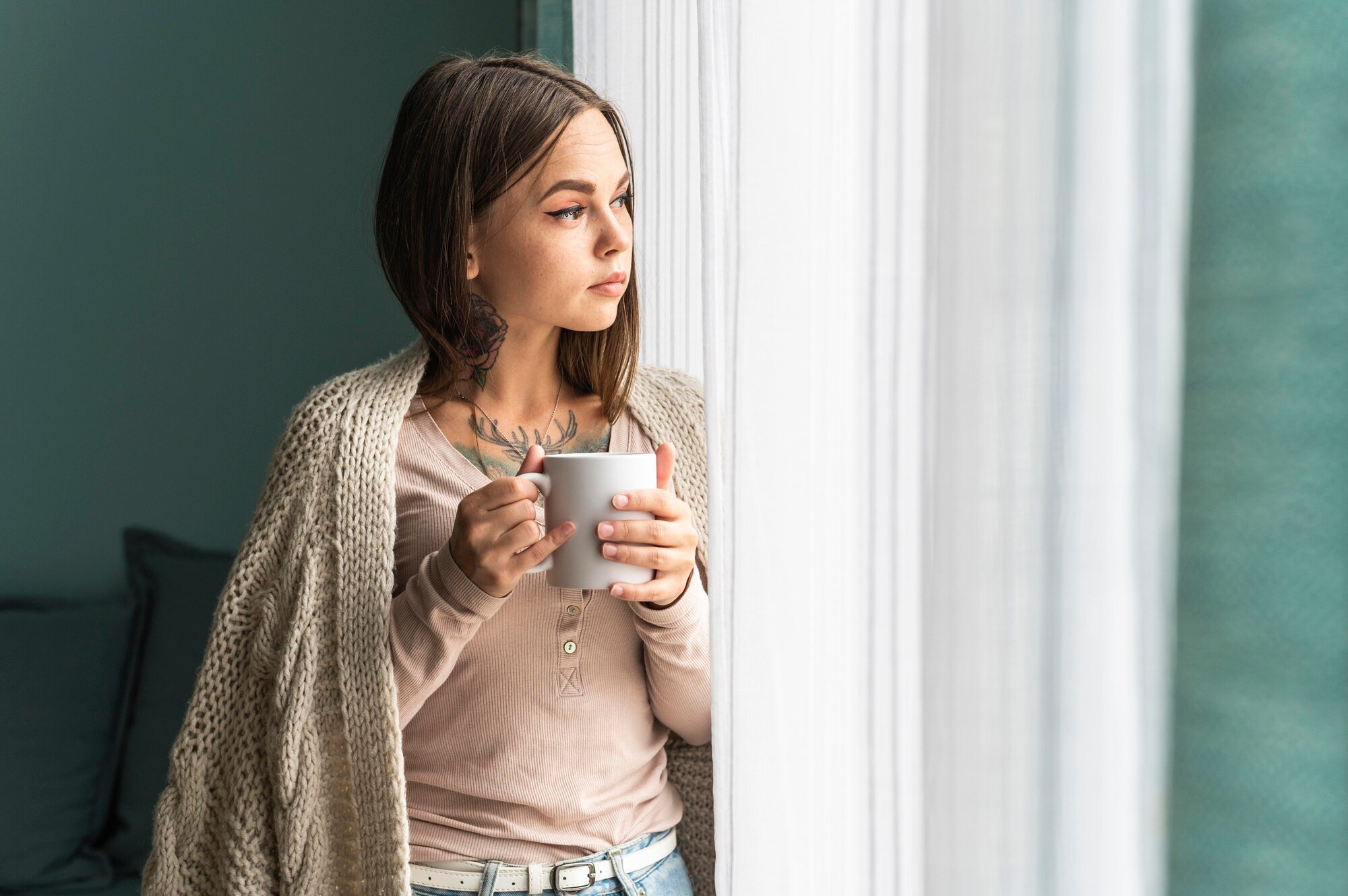 Persona en calma durante la mañana, tomando una taza de té junto a una ventana iluminada